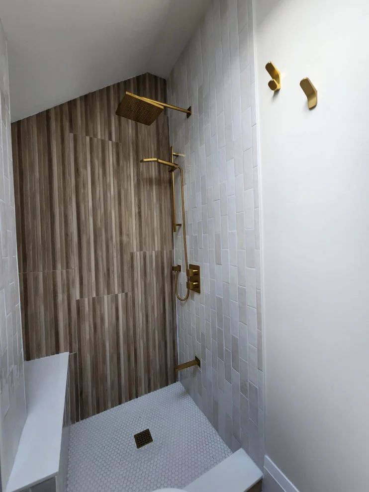 Walk-in shower with wood-grain accent wall, white tile, small bench and gold fixtures
