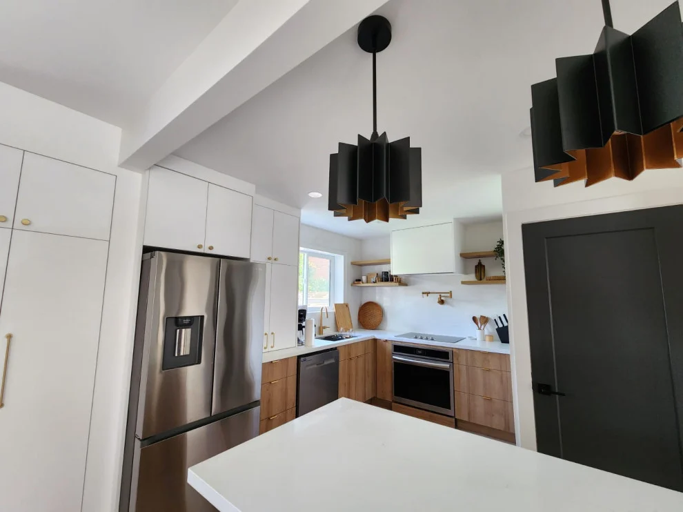 Kitchen with black flared pendants over white island, stainless fridge and wood base cabinets
