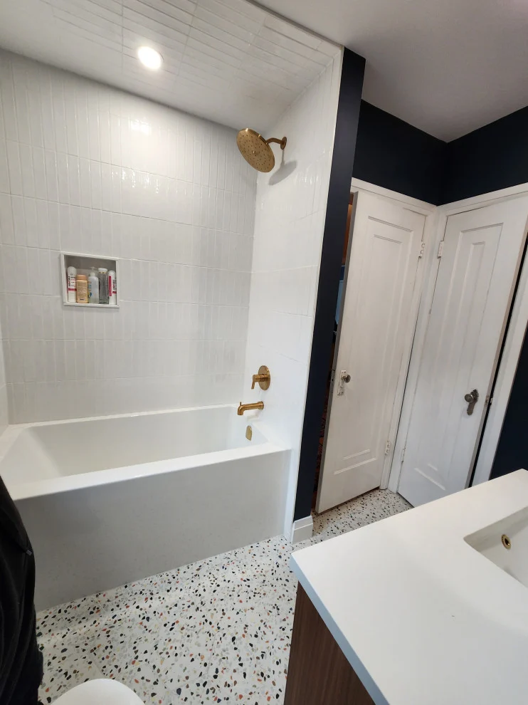 Alcove tub with white vertical tile beside white panel doors and navy walls on terrazzo floor