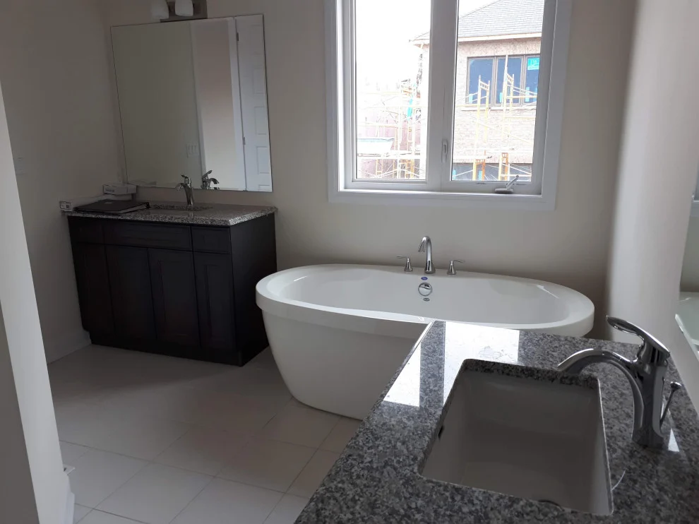 Bright bathroom with freestanding tub under window, dark vanity and granite counter in foreground