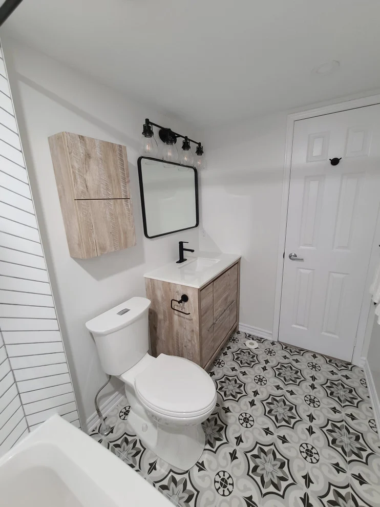 White bathroom with wood-look wall cabinet, small vanity, toilet and patterned floor tile