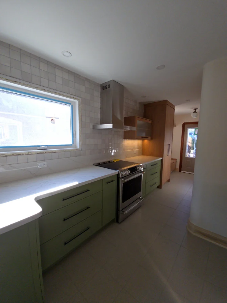 Galley view of green cabinets, white quartz counters, stainless range and window over counter