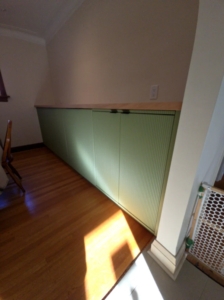 Low sage green built-in cabinets with wood top along wall above hardwood floor