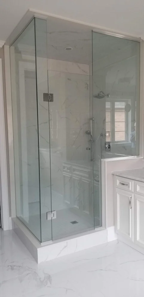 Frameless glass corner shower with marble-look tile next to a white vanity