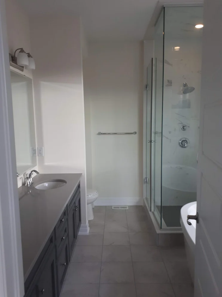 Narrow ensuite with dark vanity, frameless glass shower enclosure and tile floor