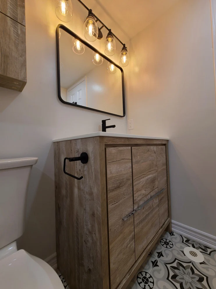 Wood-look vanity with black faucet and towel ring beneath black framed mirror and globe lights