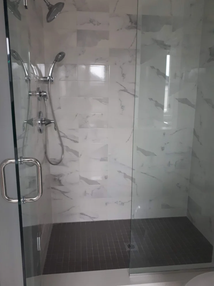 Glass shower with white marble-look tile, chrome rain head, handheld shower and dark mosaic floor