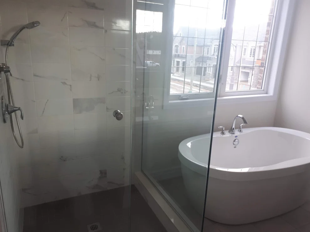 Marble-look tiled glass shower beside a freestanding white tub under a window