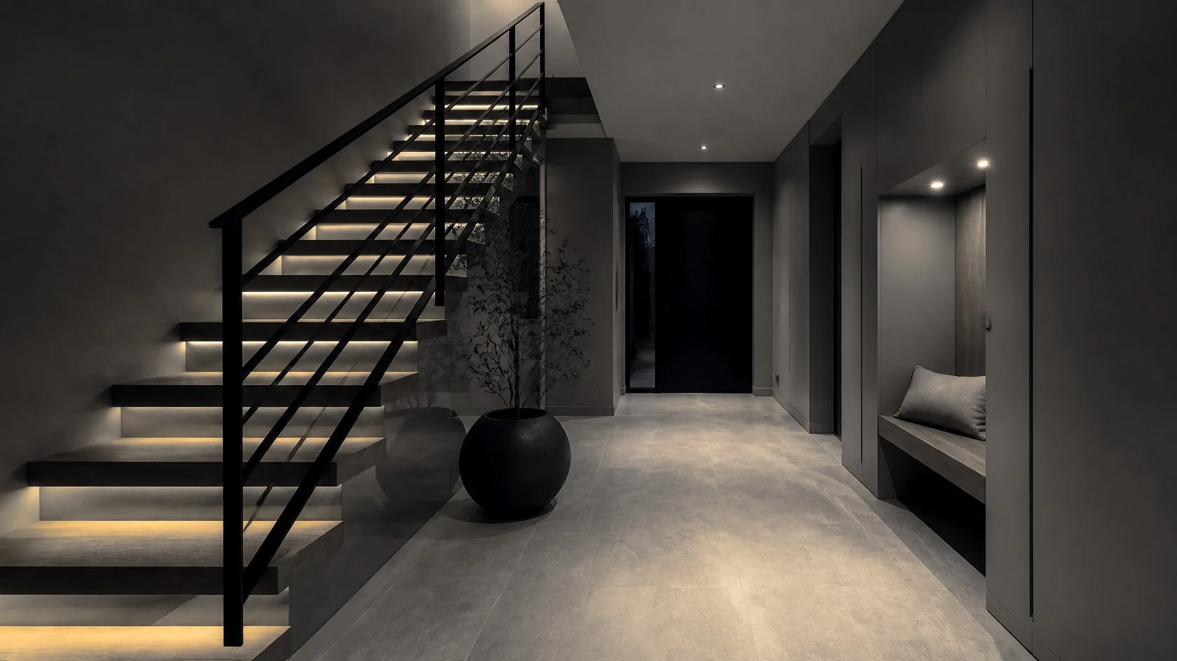 Entry hall with a floating oak staircase lit from below and a black railing